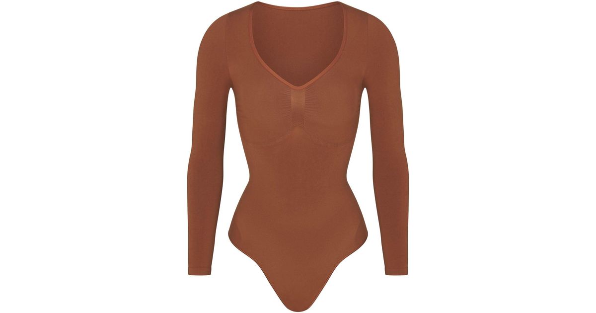 https://cdna.lystit.com/1200/630/tr/photos/skims/6e9c1fb9/skims-Bronze-Long-Sleeve-Thong-Bodysuit.jpeg