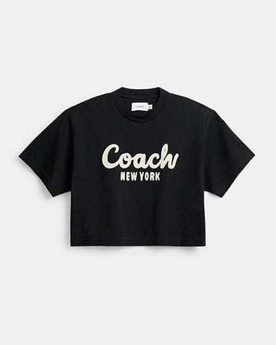 COACH Verkürztes T-Shirt mit kursiver Signature - Schwarz