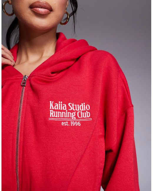 Studio - sweat à capuche court d'ensemble en coton mélangé à fermeture éclair et inscription running club Kaiia en coloris Red