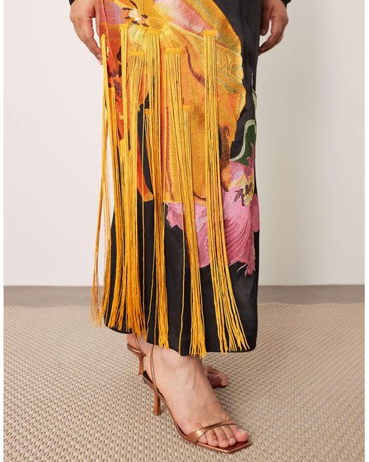 Curve - robe longue à dos ouvert et épaules marquées avec broderies fleuries et franges ARRANGE en coloris Black