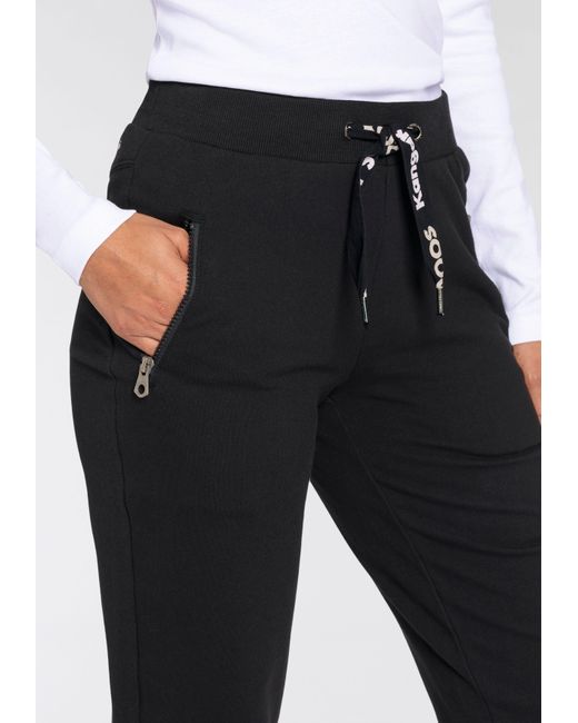 Kangaroos Jogger Pants Sweatpants Logo DE mit | -NEUE Lyst und in KOLLEKTION Schwarz Zippertaschen String